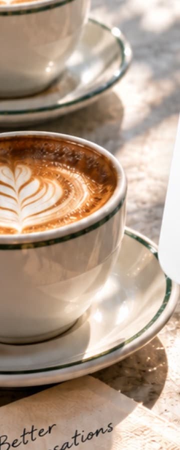 Two cappuccinos with latte art on a sunny café table